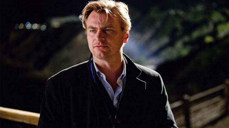 Christopher Nolan no set de Inception, vestindo um casaco e olhando para fora da câmera