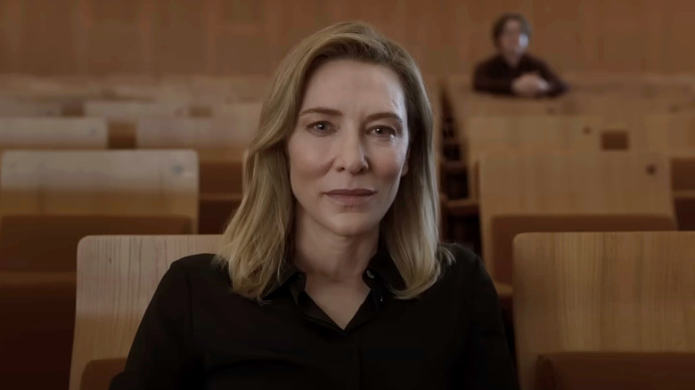 Lydia Tár, de Cate Blanchett, sentada em uma fileira de assentos de madeira olhando diretamente para a câmera em Tár