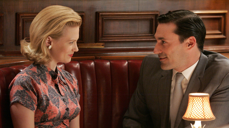 Betty Draper e Don Draper sorrindo um para o outro enquanto estão sentados em uma mesa de restaurante